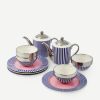 Blue and white striped porcelain tea set with pink accents, including two teapots, two teacups, and matching saucers on a white surface.