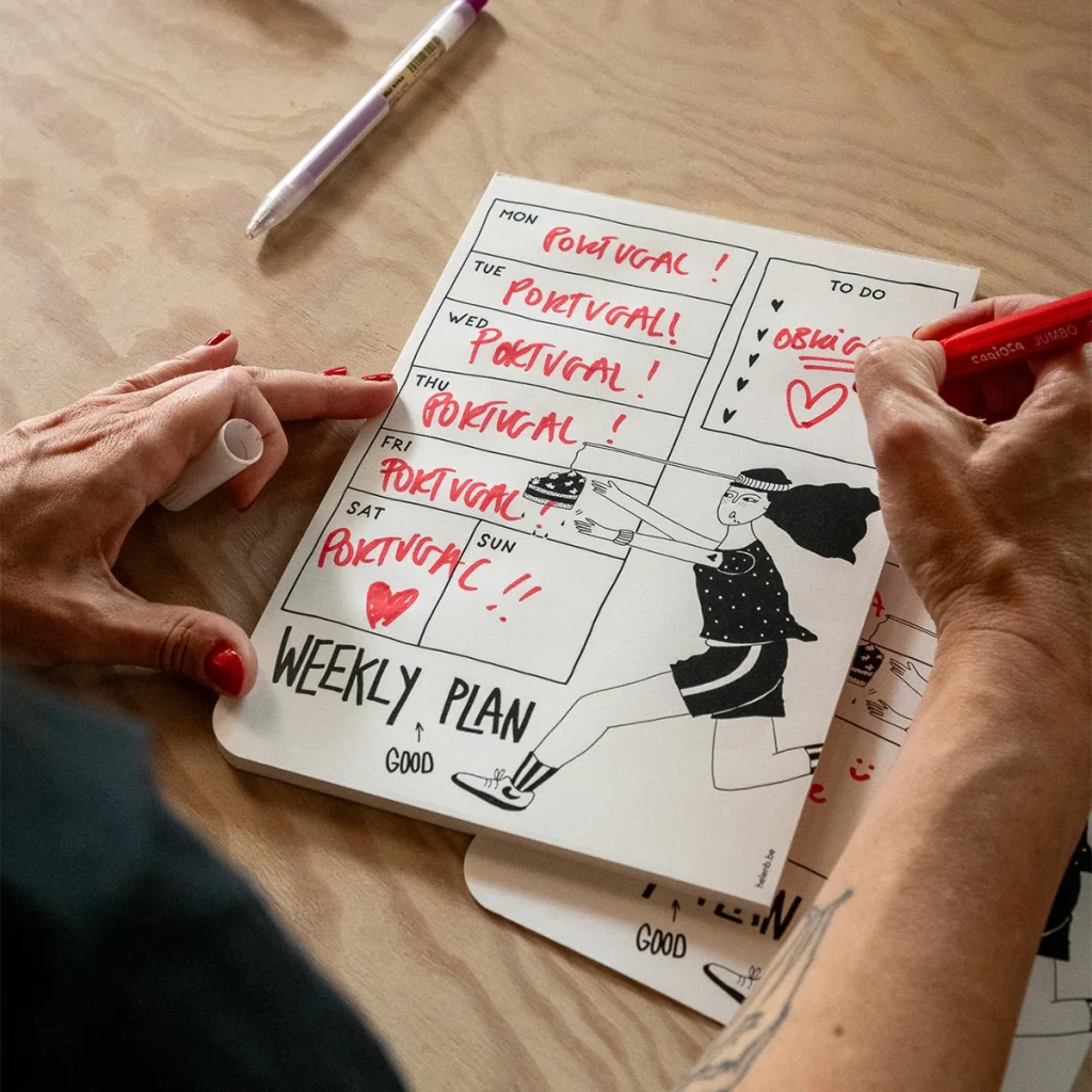 Person writes on a weekly plan page with a red marker; cartoon runner illustration appears on the page.”,