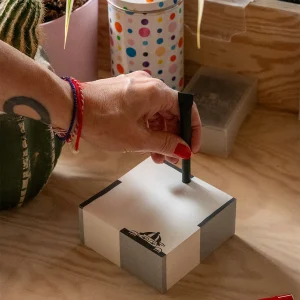 Person stamping a small white gift box with a black marker, close-up detail of the hand and box.