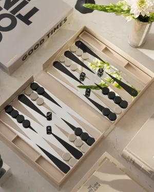 Open backgammon set with black and white checkers and dice on a light marble surface, with a flower vase nearby.