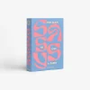 IMG_2535 - New Trend Blue hardcover book with large pink abstract typography reading 'TOO GLAM TO GIVE A DAMN' on the cover, standing upright on a white background.