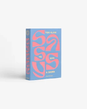 Blue hardcover book with large pink abstract typography reading 'TOO GLAM TO GIVE A DAMN' on the cover, standing upright on a white background.