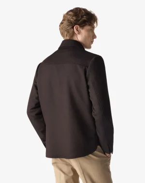 Man seen from behind wearing a dark brown jacket with a curved hem and beige pants.