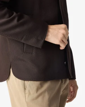 Close-up of a person wearing a dark brown blazer with a hand resting in the blazer pocket, beige pants visible below.