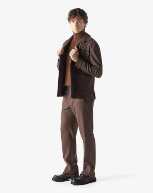Male model in a brown turtleneck and brown suit, adjusting his jacket and looking at the camera.