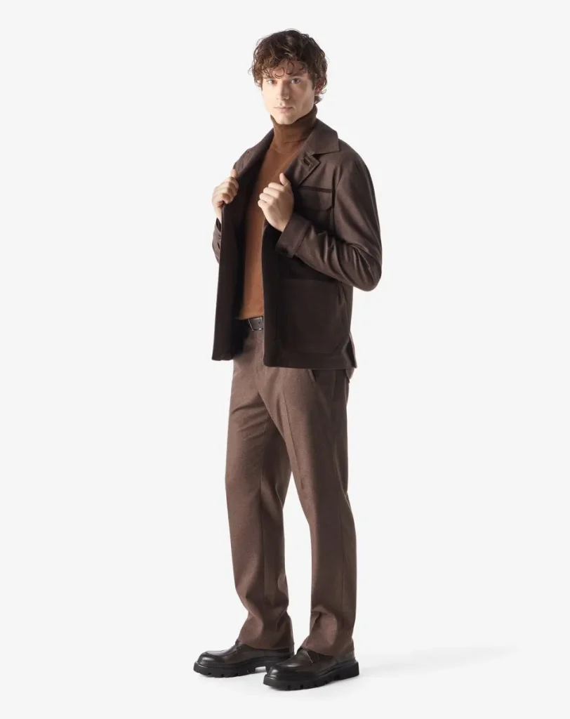 Male model in a brown turtleneck and brown suit, adjusting his jacket and looking at the camera.