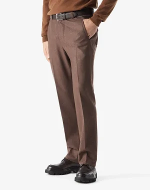 Full-length view of a person wearing brown dress pants with a black belt, brown sweater, and black chunky loafers; one hand in the pocket.