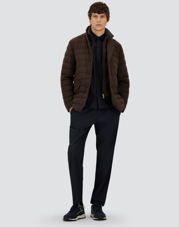 Man wearing a brown quilted jacket over a navy outfit with dark sneakers, posing in a full-body fashion shot