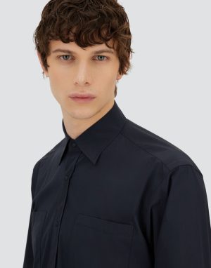 Young man wearing a dark navy button-down shirt, looking slightly to the side against a light gray background.