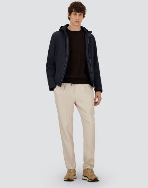 Male model wearing a navy zip-up jacket, black sweater, beige chinos, and tan sneakers against a light background.