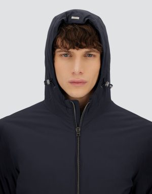 Close-up of a person in a navy hooded jacket with a zip front, looking at the camera against a light gray background.