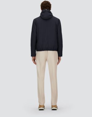 Back view of a person in a navy hooded jacket and beige trousers on a light gray backdrop.