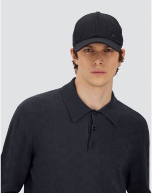 Model wearing a dark textured polo shirt and a black cap against a light gray background.