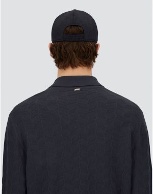 Back view of a person wearing a dark textured polo shirt and a navy cap, showing a small metal collar tag.