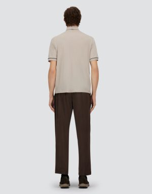 Man seen from behind wearing a beige short-sleeve polo and dark brown pants, standing against a light gray background, with brown shoes visible below.