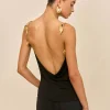 Back view of a woman wearing a black halter top with a low open back, gold leaf earrings, and a tight bun hairstyle.