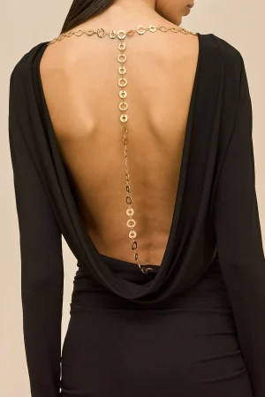 Back view of a person wearing a black open-back dress with a gold circular-link necklace draping down the spine.