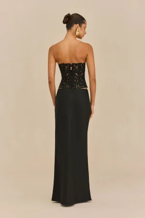 Rear view of a woman in a black lace strapless top and long black skirt, hair in a bun and a large gold earring.