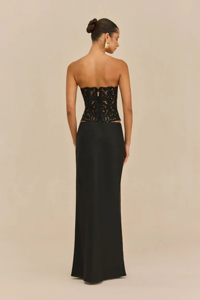 Rear view of a woman in a black lace strapless top and long black skirt, hair in a bun and a large gold earring.