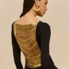 Side profile of a woman in a black dress with gold layered back panels and a large gold hoop earring beneath her ear.