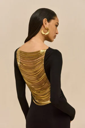 Side profile of a woman in a black dress with gold layered back panels and a large gold hoop earring beneath her ear.