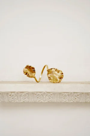 Gold bracelet with two large leaf-shaped charms resting on a light display pedestal.