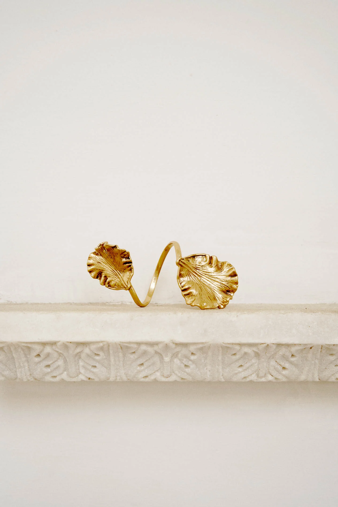 IMG_2593 - New Trend Gold bracelet with two large leaf-shaped charms resting on a light display pedestal.