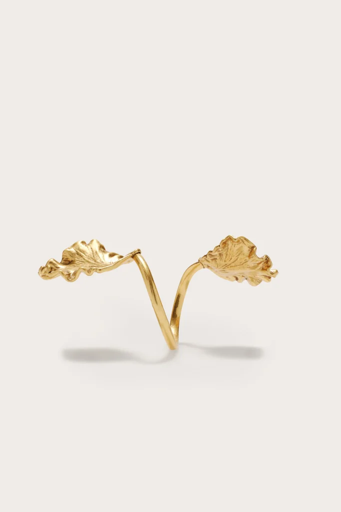 Gold ring with two leaf-shaped branches forming an open, nature-inspired design on a light backdrop