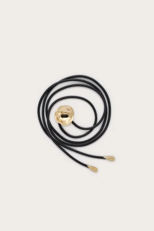 Black cord necklace with a hammered gold circular pendant lying on a pale background, coils visible.