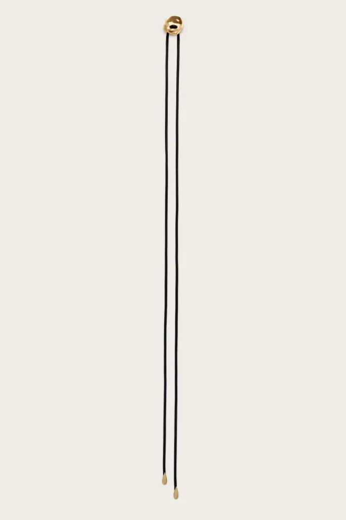 Two black cords hanging vertically with gold teardrop beads at their ends against a light background.