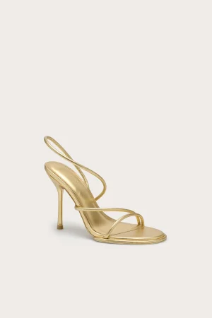 Gold high-heeled sandal with thin straps and open toe on a pale beige background (close-up side view).