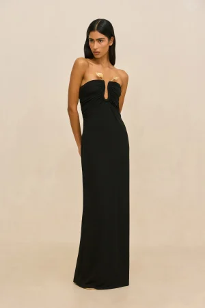 Full-length portrait of a woman in a black strapless gown with gold leaf accents at the bust against a beige backdrop.