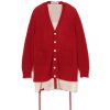 Red chunky knit cardigan with white buttons worn over a cream pinstriped dress, featuring two front pockets and long ties visible at the hem.