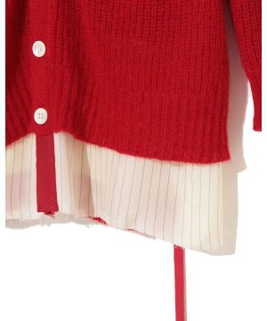 Close-up of a red knit sweater layered over a white striped shirt with red ribbon hanging down and white buttons visible on the cuff.