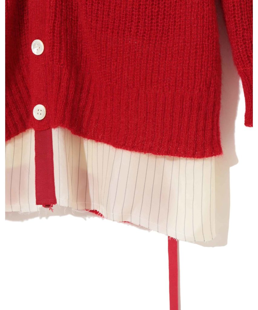 Close-up of a red knit sweater layered over a white striped shirt with red ribbon hanging down and white buttons visible on the cuff.
