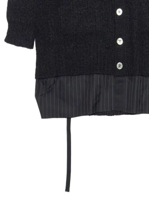 Close-up of a black textured knit cardigan with white buttons over dark pinstriped fabric underneath.