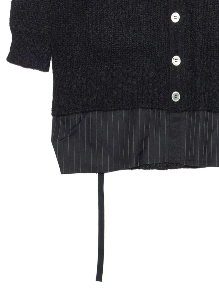 Close-up of a black textured knit cardigan with white buttons over dark pinstriped fabric underneath.