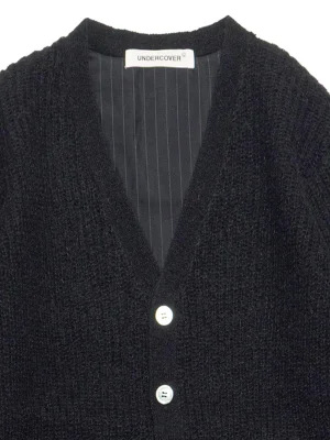 Close-up of a black knit cardigan with a striped inner lining and three white buttons, label reads UNDERCOVER.