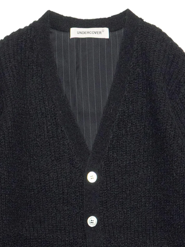 Close-up of a black knit cardigan with a striped inner lining and three white buttons, label reads UNDERCOVER.