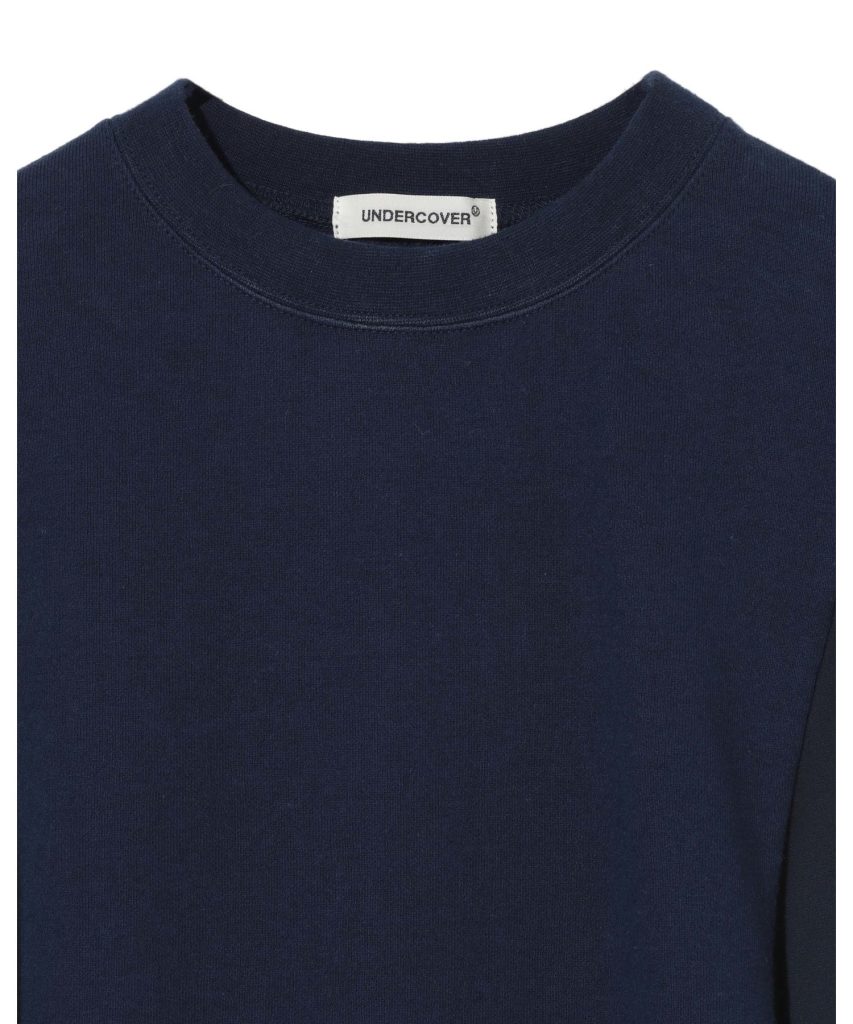 Close-up of a navy blue crew-neck T-shirt showing a white tag that reads UNDERCOVER at the back of the neck.