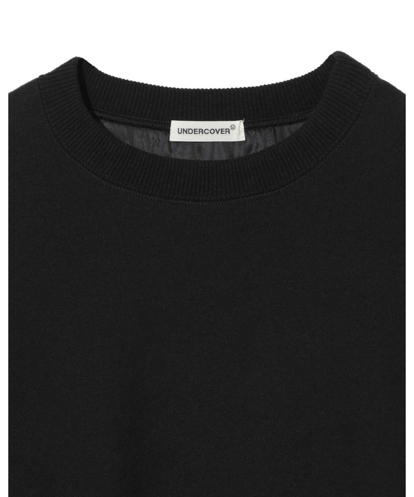 Close-up of a black crewneck neckline with a white 'UNDERCOVER' brand tag sewn inside