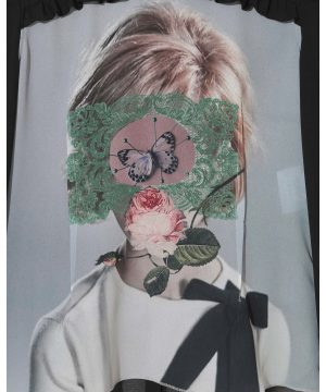 Artistic portrait: a person wearing a white shirt with a green lace mask over their face, featuring a butterfly centerpiece and pink rose at the neck.