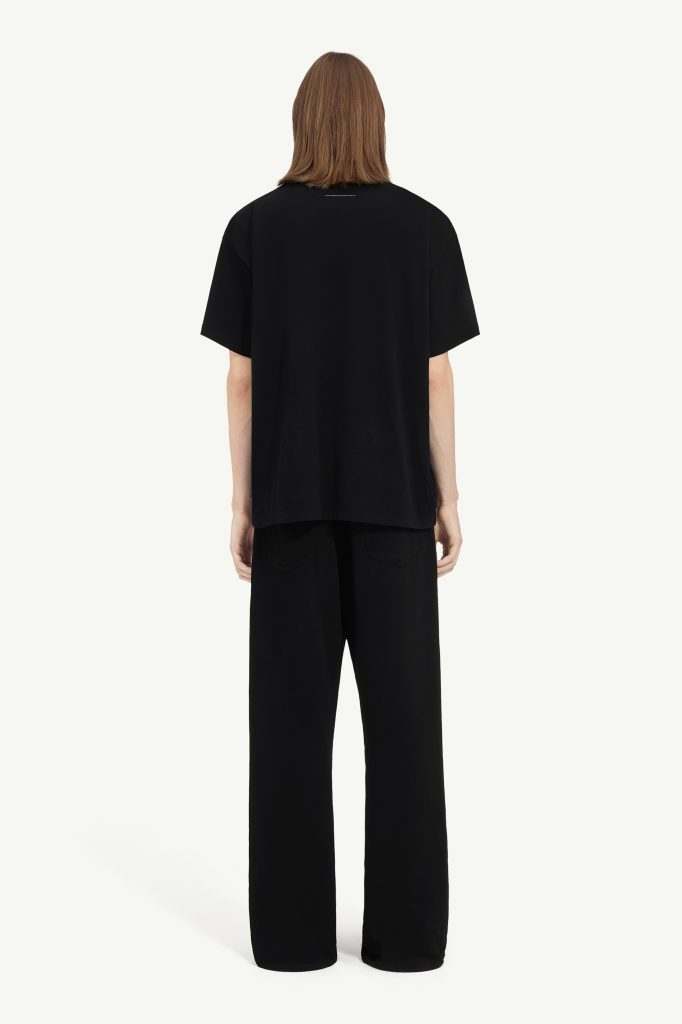 Back view of a person wearing a loose black T-shirt and wide-leg black pants, with shoulder-length brown hair, neutral background.