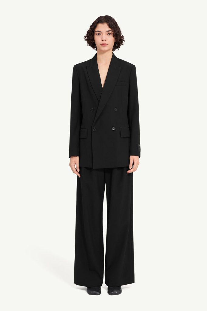 Full-length image of a person in a black oversized double-breasted blazer with wide-leg trousers against a light background.