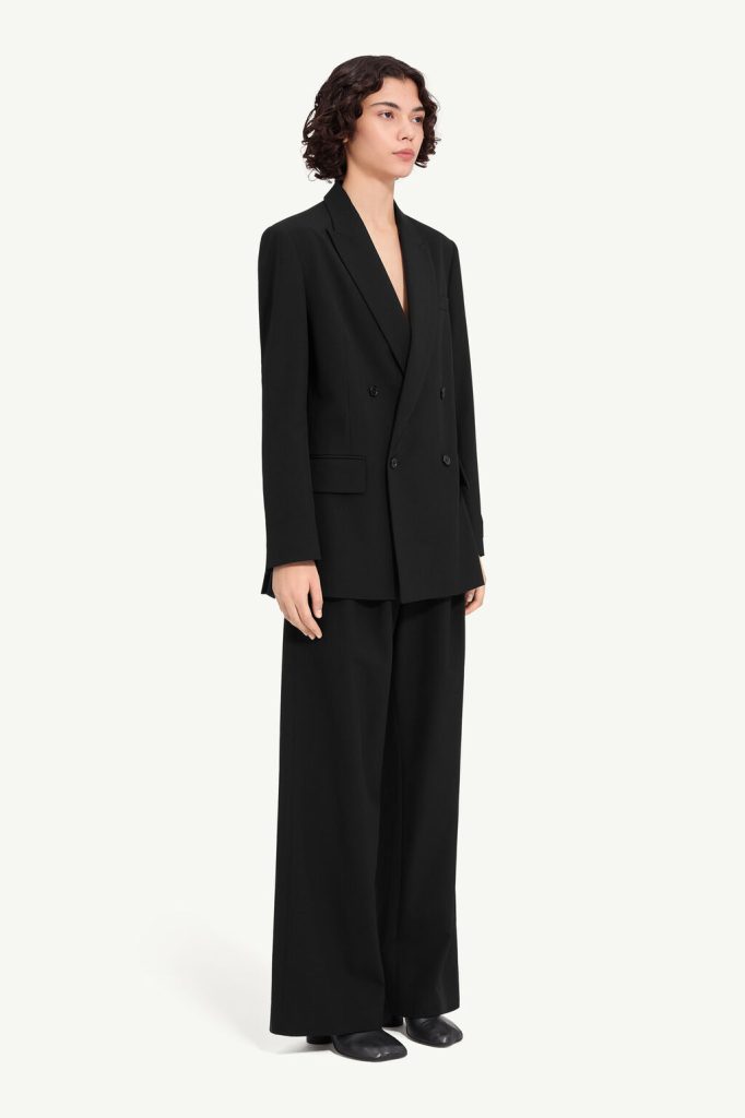Model wearing an oversized black double-breasted blazer with matching wide-leg trousers and black shoes against a pale background.