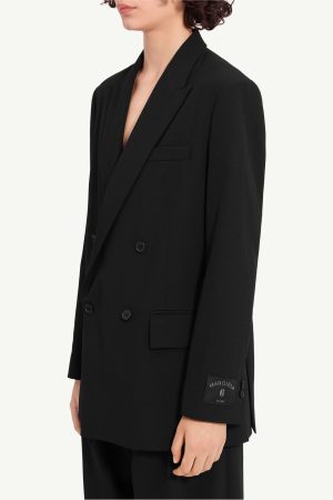 Person wearing a black double-breasted blazer with peak lapels; cuff features a Margiela label reading 'Margiela 6 EST 1987'