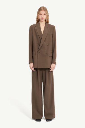 Model in an oversized brown double-breasted blazer with wide-leg matching trousers, black shoes, neutral studio backdrop
