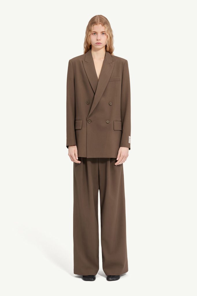 Model in an oversized brown double-breasted blazer with wide-leg matching trousers, black shoes, neutral studio backdrop