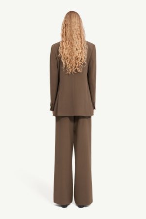 Person with long curly blond hair wearing a brown blazer and wide-leg pants, viewed from the back.