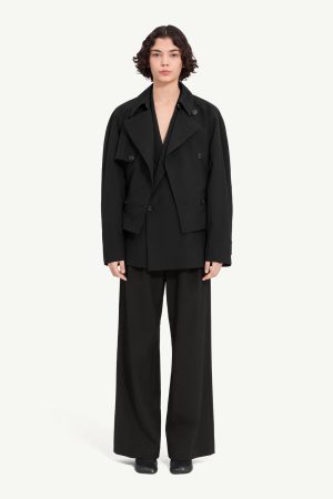 Person wearing an oversized black blazer over a matching black suit with wide-leg trousers, facing the camera against a light background.